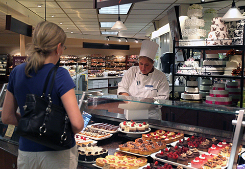 A customer ordering cupcakes from a staff member in a chef's hat behind the pastry counter.