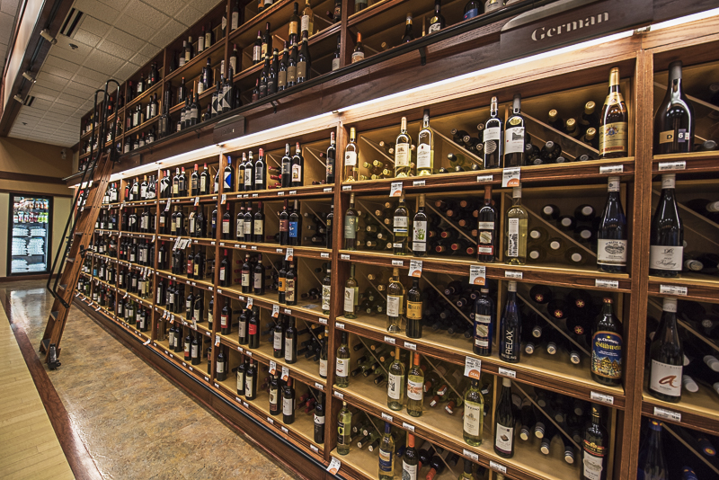 a fancy shelf full of wine bottles with a rolling ladder on a rail to reach the higher shelves.