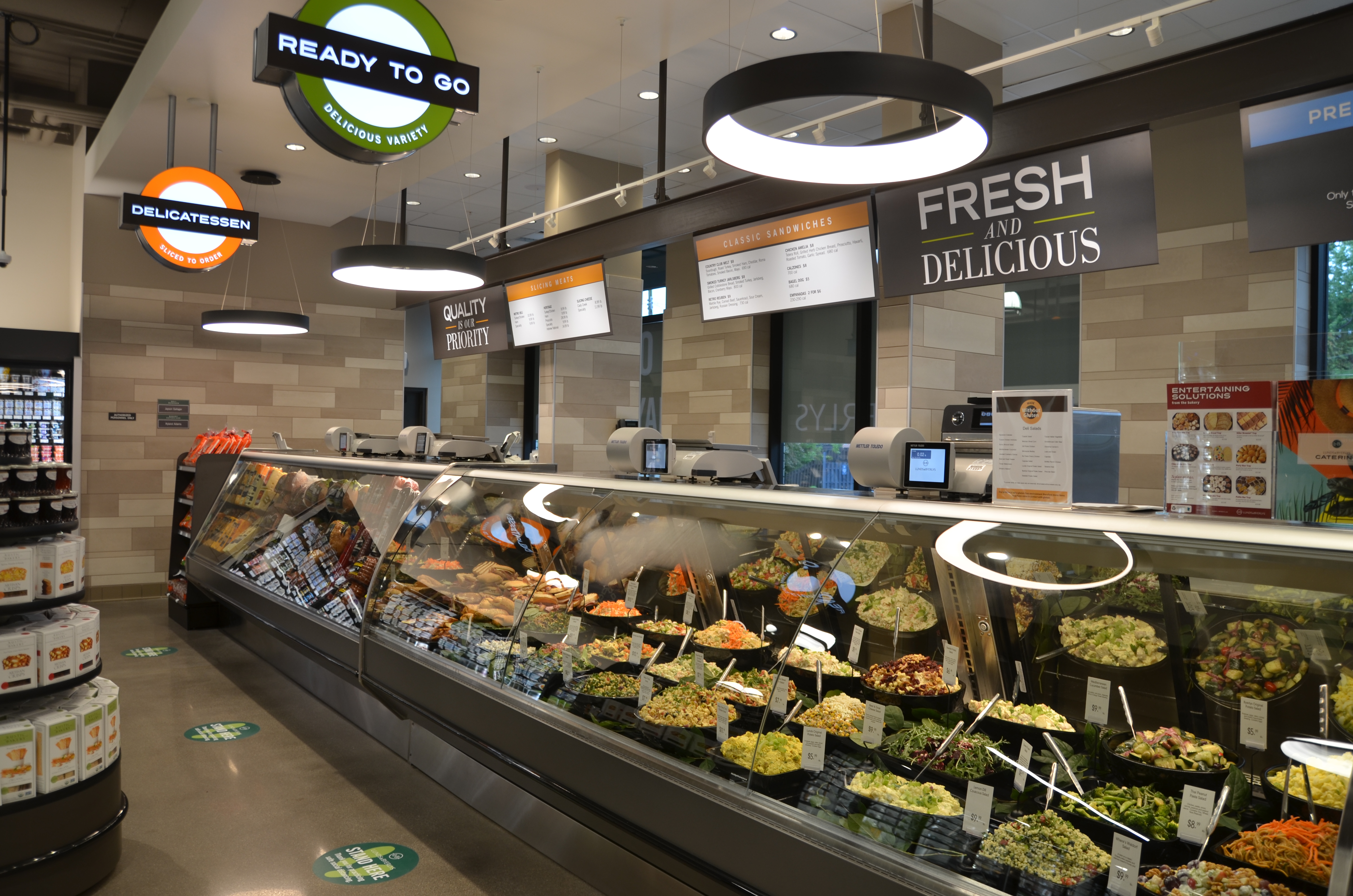 A deli section with a Fresh And Delicious sign and a Ready To Go sign.